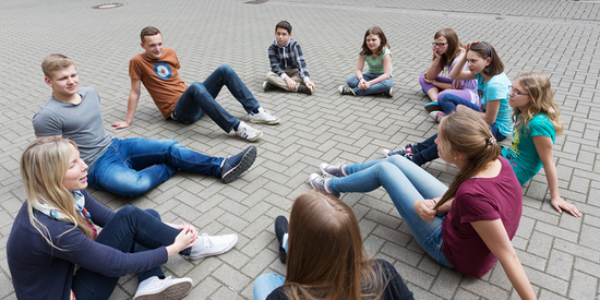 Jugendliche sitzen im Kreis auf dem Schulhof.