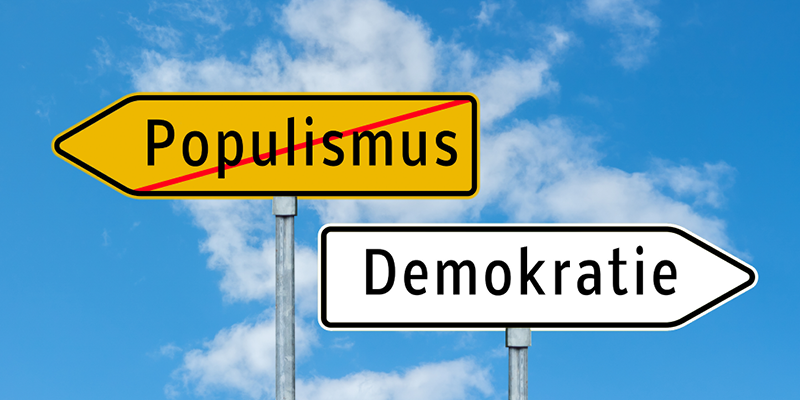Zwei Schilder mit der Aufschrift Demokratie und Populismus, was durchgestrichen ist.